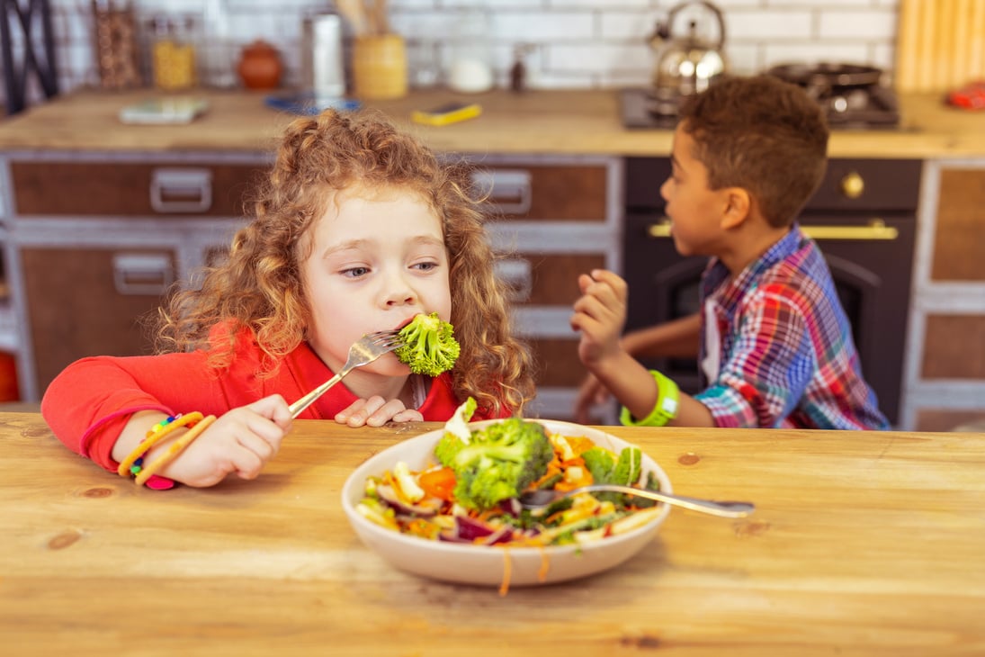 Hungry curly-haired kid eating healthy food for dinner